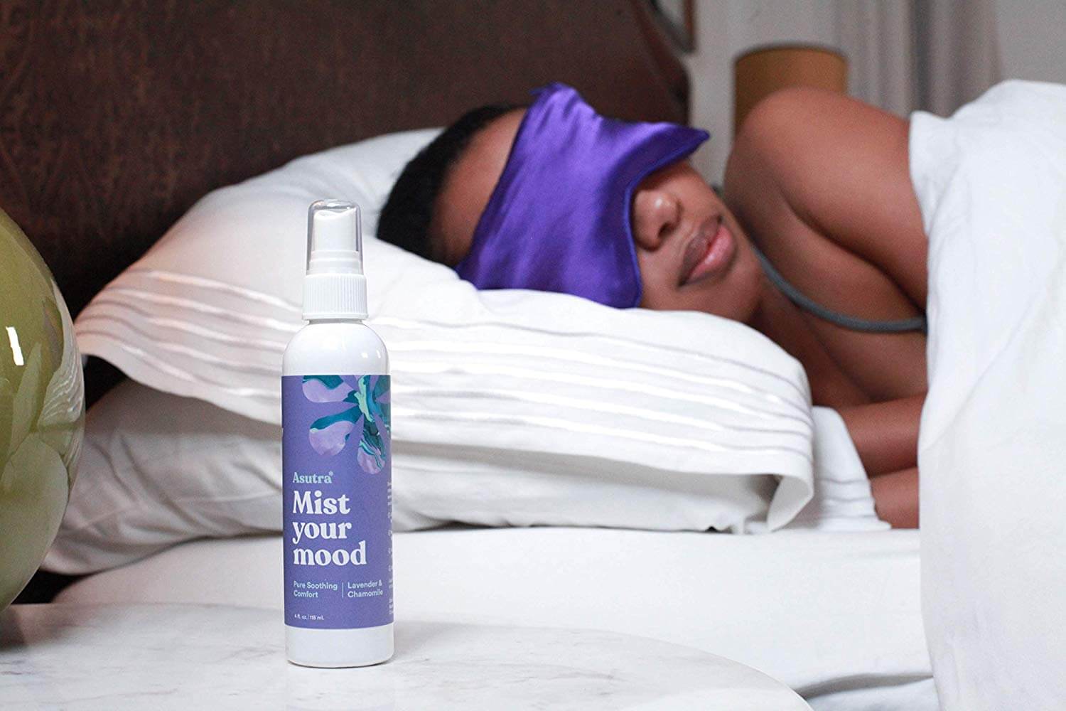 A woman is sleeping next to "Mist your mood" pillow spray by Asutra
