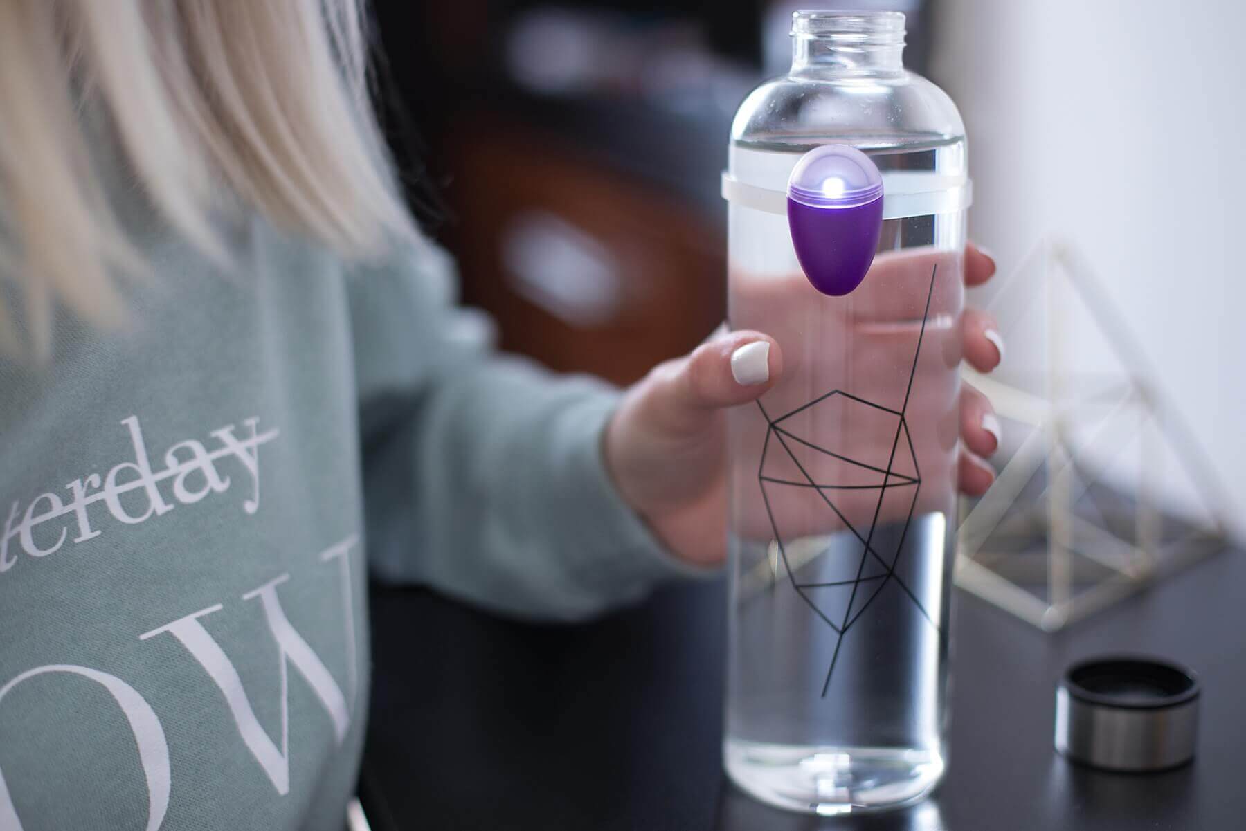 A blonde girl holding a plastic water bottle with an electronic reminder device on it