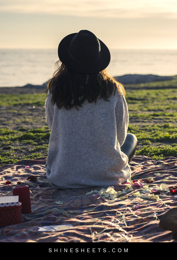 young woman with a hat practicing emotional self care by sitting by the sea