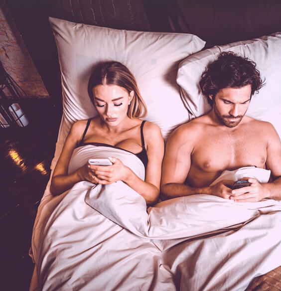 couple in bed playing with phones and experiencing retroactive jealousy