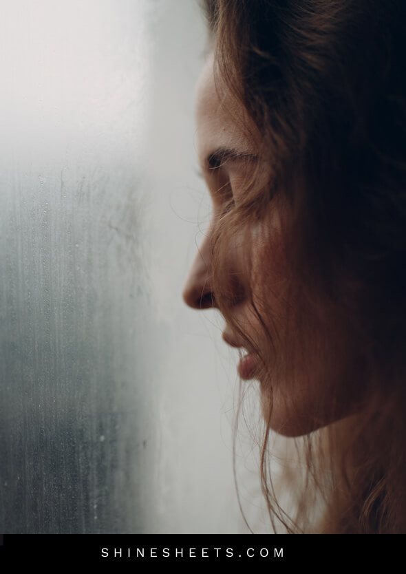 sad woman looking through the window into the rain
