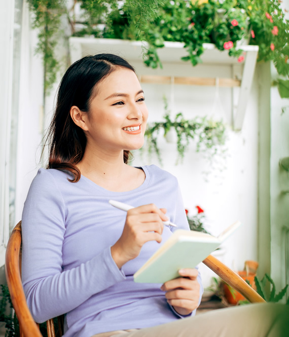 smiling asian woman writes down her life goals examples in a notebook