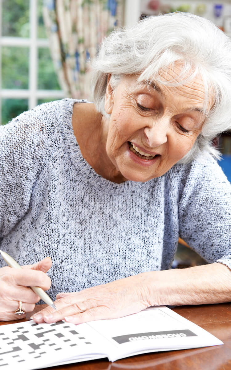 an elderly woman doing crossword puzzle for memory care