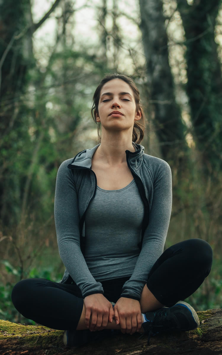 woman meditating in the forest to soothe ovearctive mind