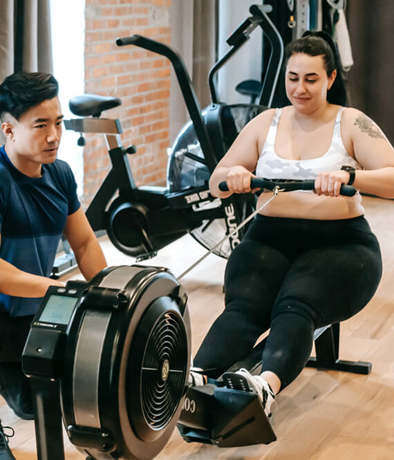 personal trainer teaches young person how to use a rowing machine