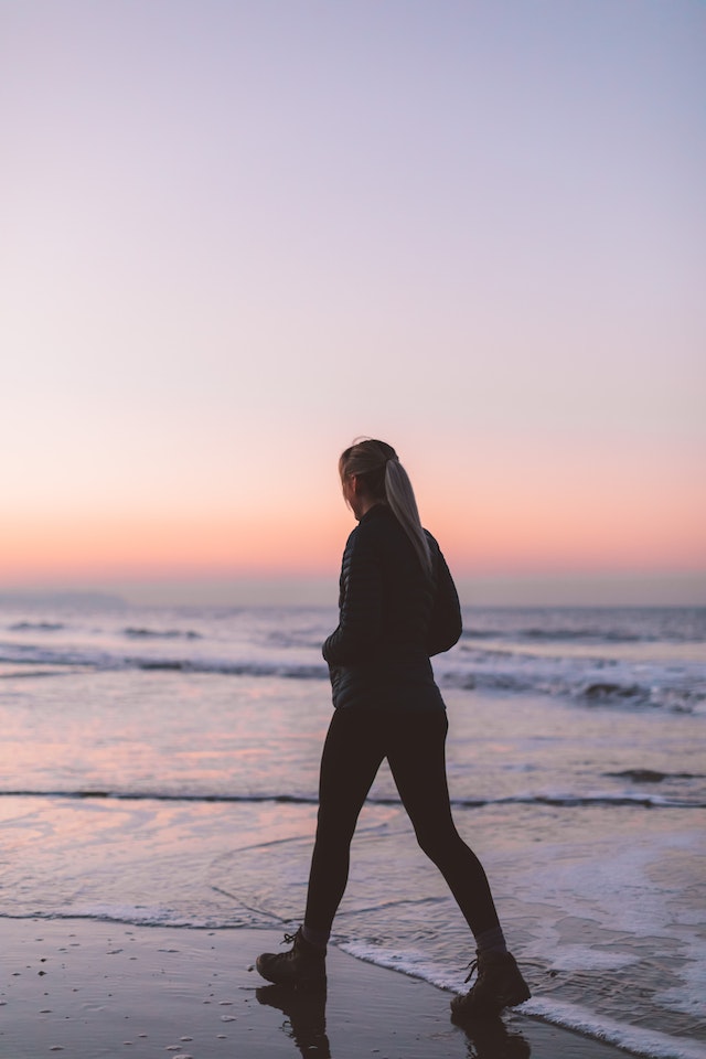 woman taking a mindful walk on the beach in the evening, when the sun is setting