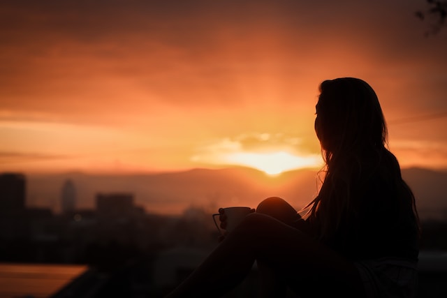 woman watching a sunset on a rooftop with a drink in her hand, mindfully pausing