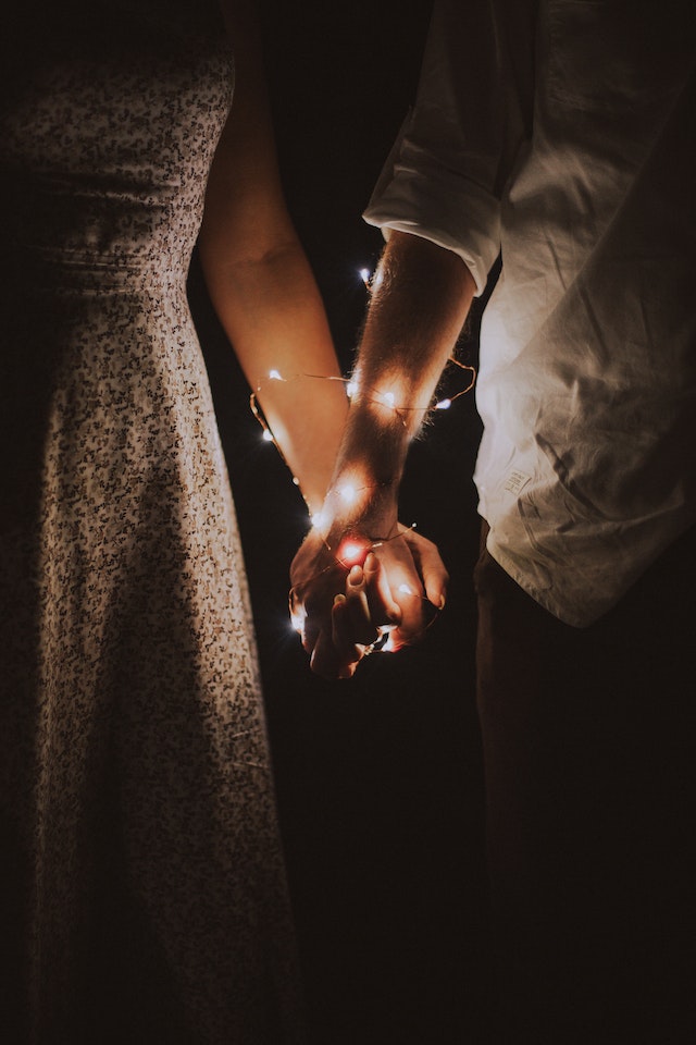 a couple holding hands that have christmas lights wrapped around them, posing for a christmas card
