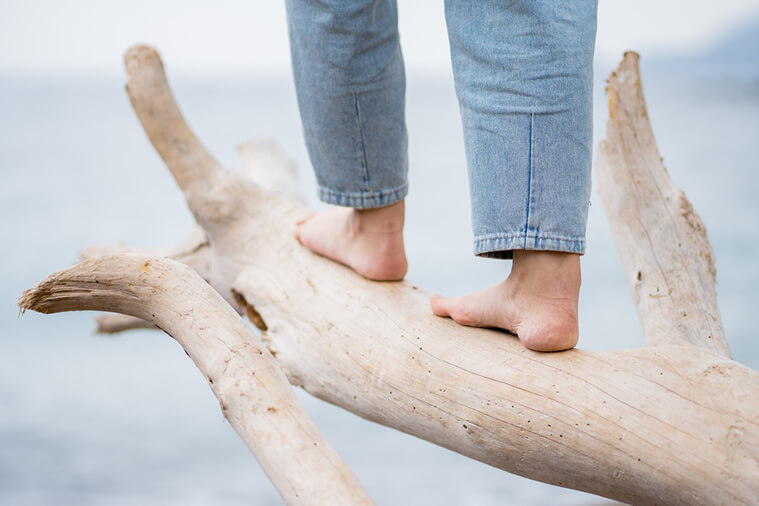 woman tip-toeing on a wood log for health benefits of walking barefoot