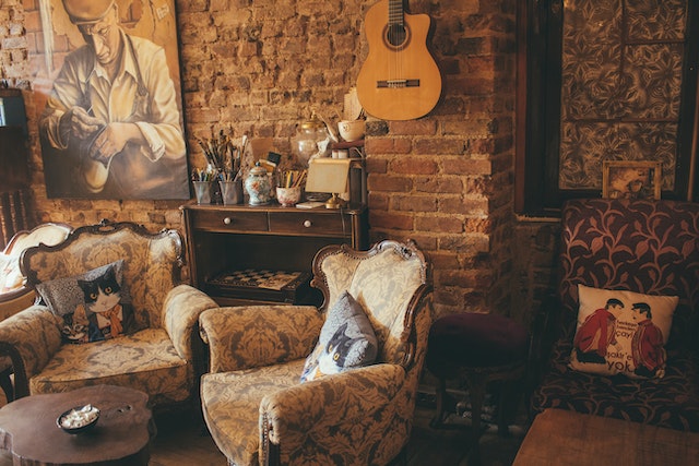 two brown chairs in a living room that is built around a rustic art theme, with a guitar hanging on the wall