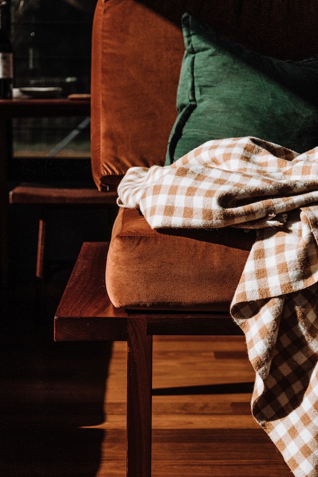 a brown sofa in a living room with a blanket and pillows and natural light falling onto the sofa