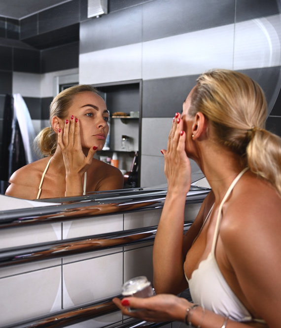 middle aged woman applying anti-aging face cream in front of the mirror
