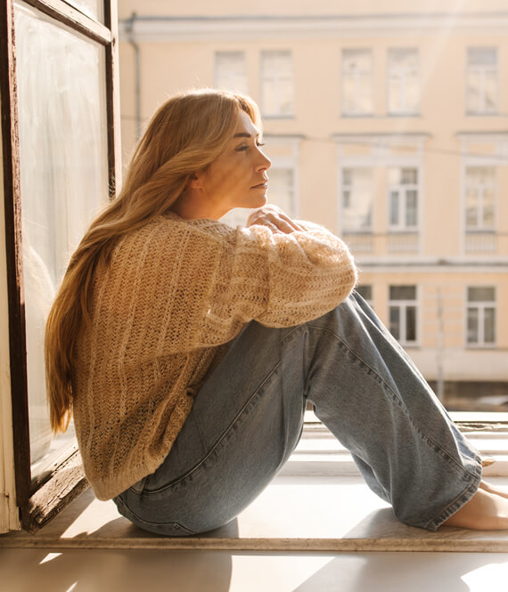 sad depressed woman sitting on the windowsill