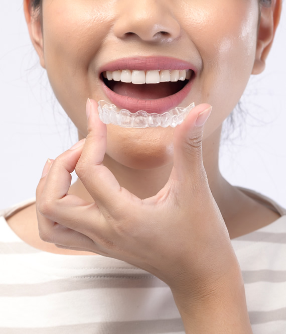 smiling woman holding invisalign braces near her mouth