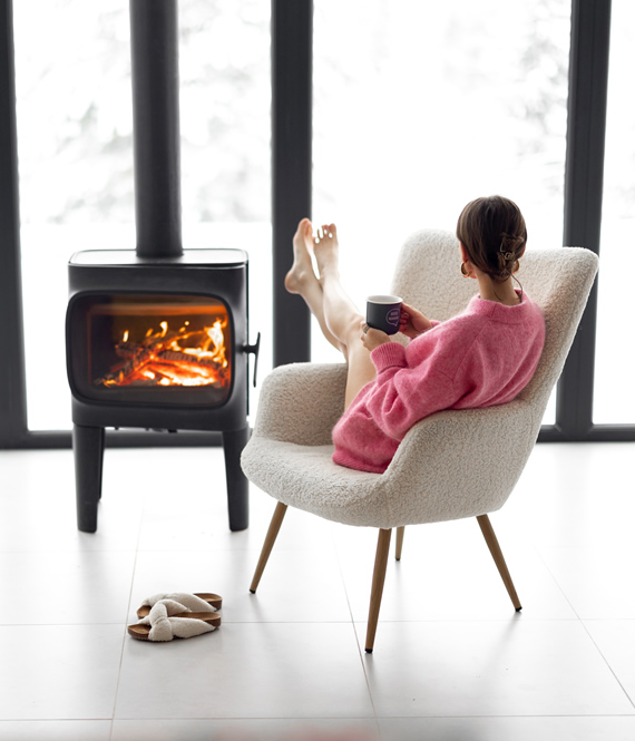 woman sits in a cozy room after installing a log burner