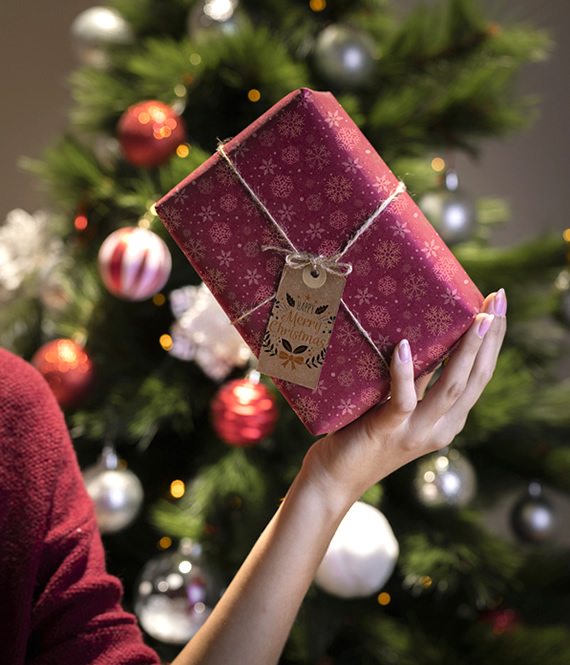 person holds expensive holiday gift in front of festive Christmas tree