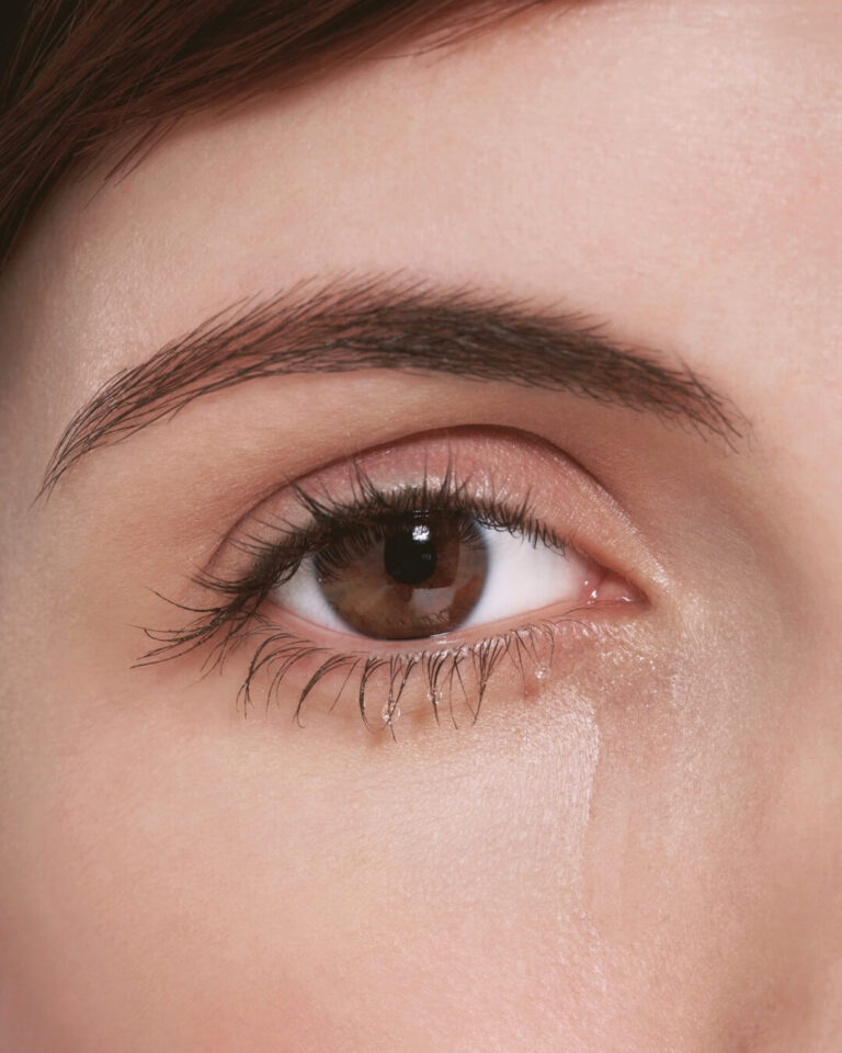 Woman with long eyelashes is crying and the tear is falling