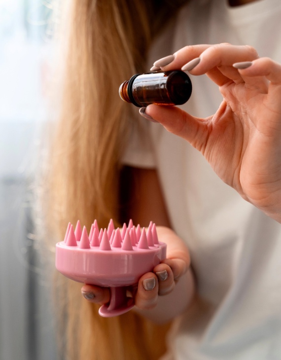 Woman demonstrates how to take cair of your hair roots with scalp massager and rosemary essential oil